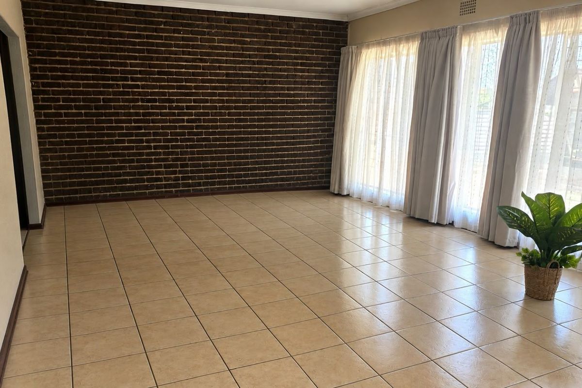 Spacious living area featuring a distinctive exposed brick wall, neutral ceramic floor tiles, and large sliding glass doors providing ample natural light.