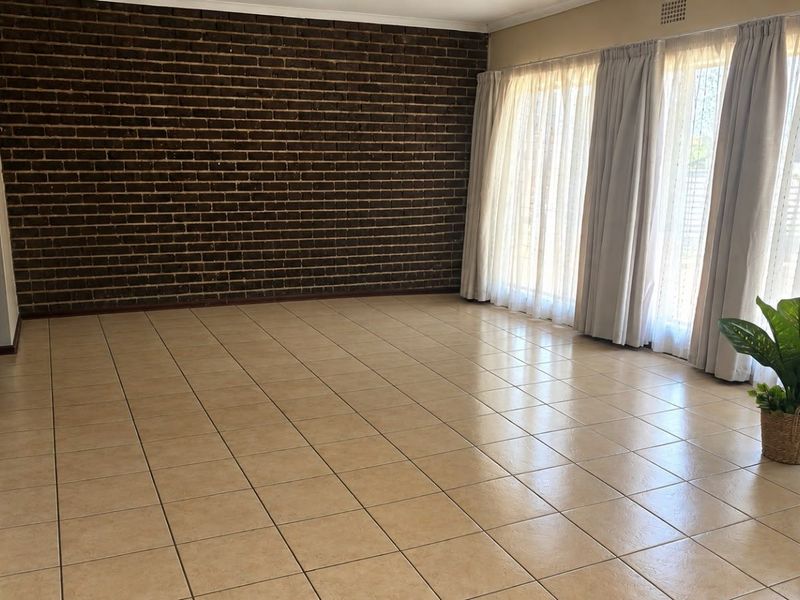 Spacious living area featuring a distinctive exposed brick wall, neutral ceramic floor tiles, and large sliding glass doors providing ample natural light.