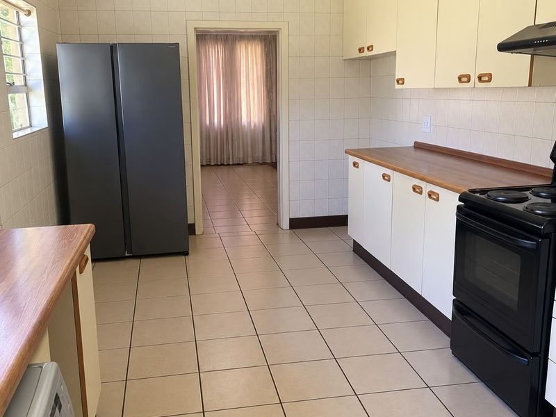 A functional kitchen featuring tiled walls and floors, built-in cabinetry with laminate countertops, and an integrated extractor fan.