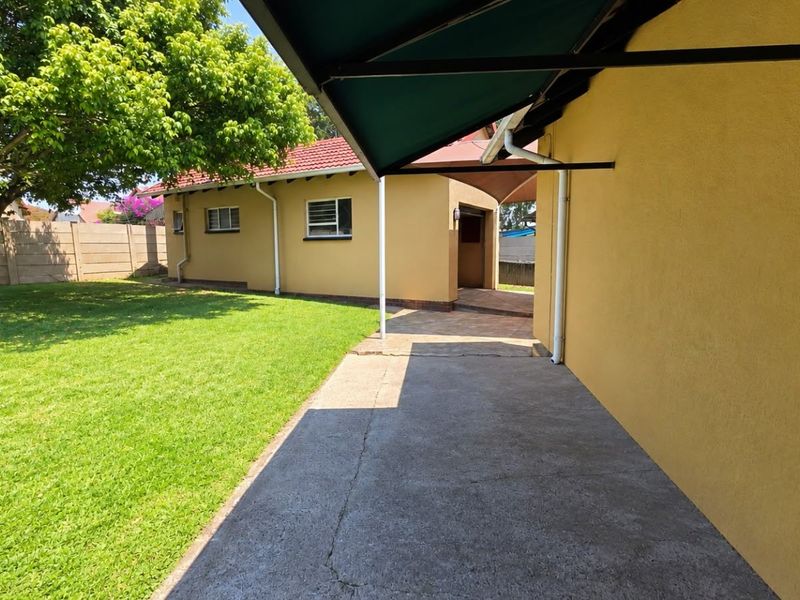 Rear exterior view featuring a concrete patio with a retractable awning, overlooking a well-maintained garden and boundary wall.