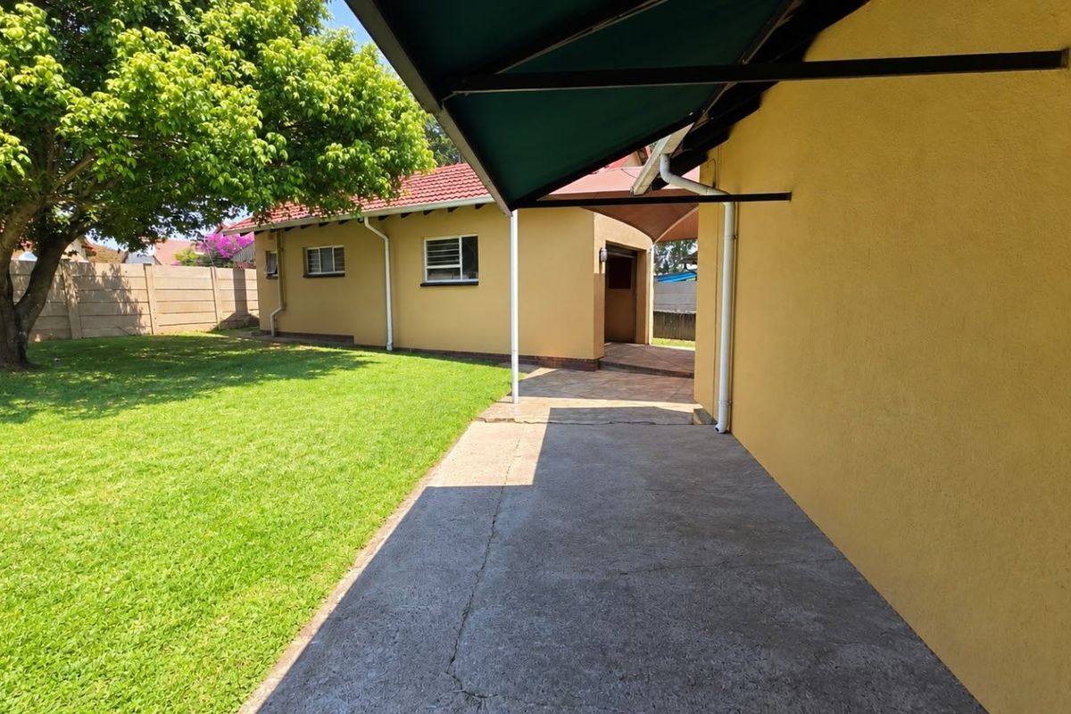 Rear exterior view featuring a concrete patio with a retractable awning, overlooking a well-maintained garden and boundary wall.
