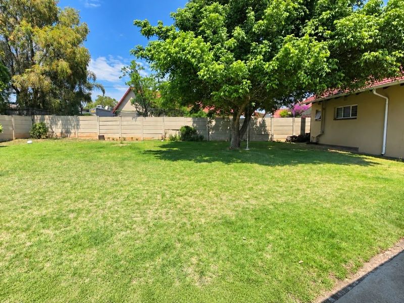 A spacious rear garden featuring a well-maintained lawn, mature tree, and secure precast concrete boundary walling.