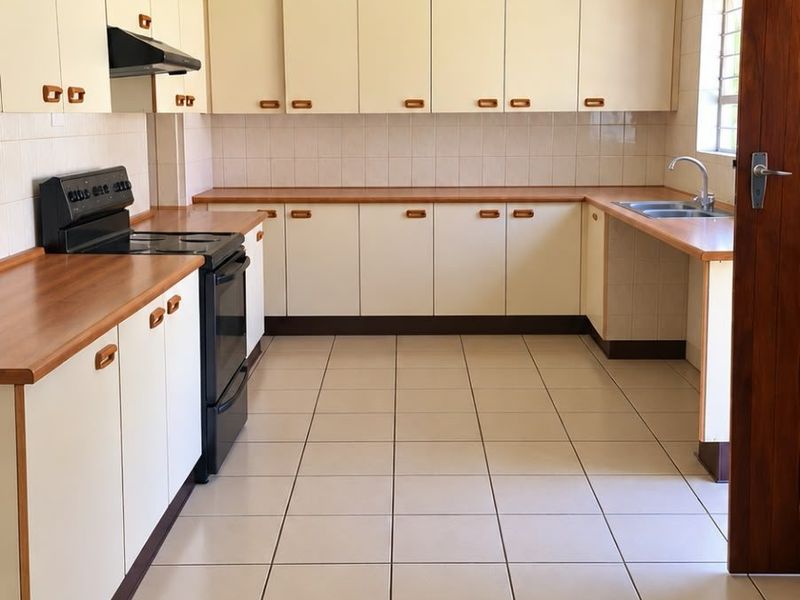 A clean, functional kitchen featuring ample laminate countertops, built-in cabinetry, tiled splashbacks, and ceramic floor tiles, offering a practical layout for daily use.