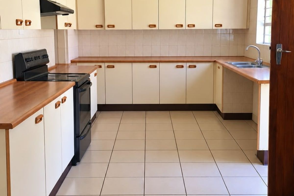 A clean, functional kitchen featuring ample laminate countertops, built-in cabinetry, tiled splashbacks, and ceramic floor tiles, offering a practical layout for daily use.