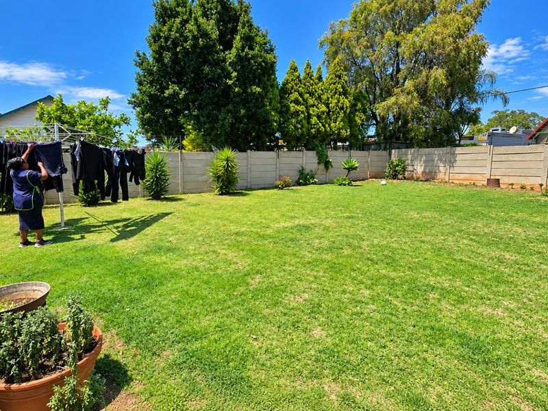 A spacious, well-maintained private backyard featuring a large lawn area enclosed by secure precast concrete boundary walls.