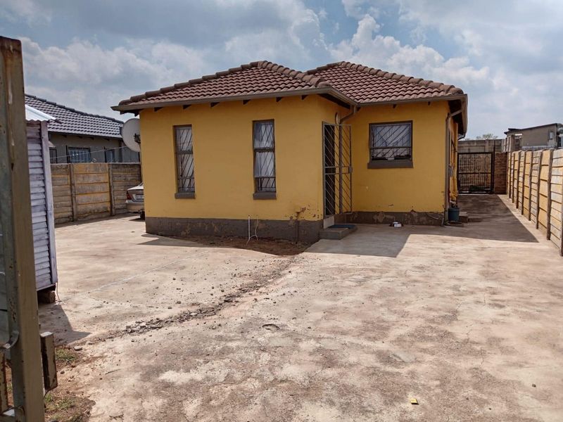 Rear view of a detached house featuring a concrete driveway, precast boundary walls, and security features on windows and doors.