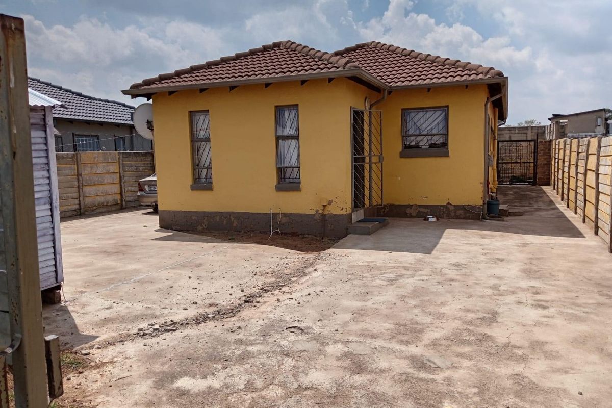 Rear view of a detached house featuring a concrete driveway, precast boundary walls, and security features on windows and doors.