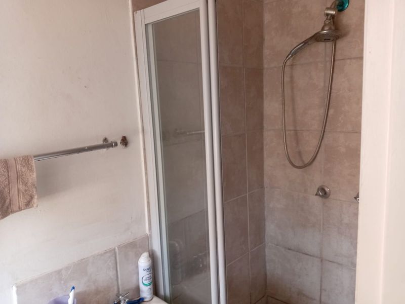 A functional bathroom featuring a tiled shower enclosure and a wall-mounted towel rail, showing signs of wear and requiring minor maintenance.