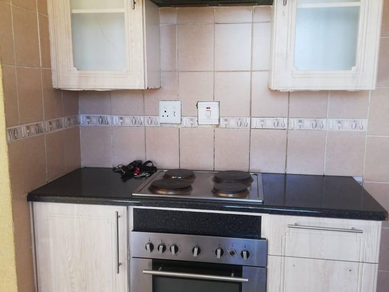 A functional kitchen area featuring built-in cabinetry, a stainless steel oven with electric hob, extractor fan, and tiled backsplash.