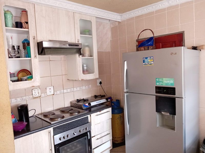 A functional kitchen featuring built-in cabinetry, an electric hob, oven, extractor fan, and tiled backsplash with granite countertops.