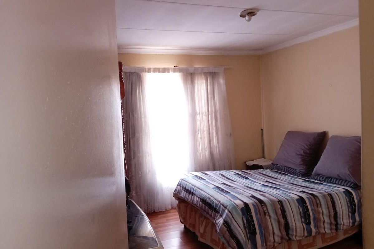 A compact bedroom featuring laminate flooring and basic ceiling finishes, offering a functional space that could benefit from cosmetic updates.