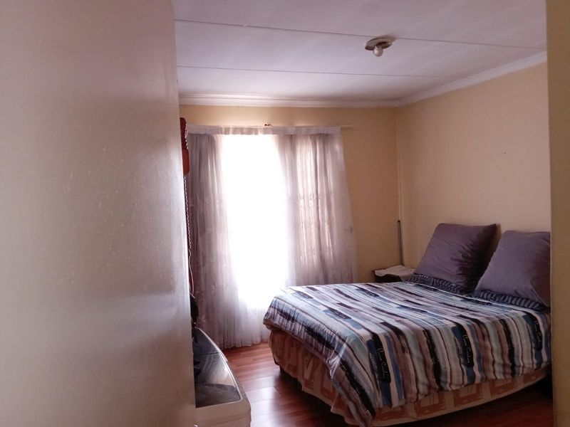 A compact bedroom featuring laminate flooring and basic ceiling finishes, offering a functional space that could benefit from cosmetic updates.