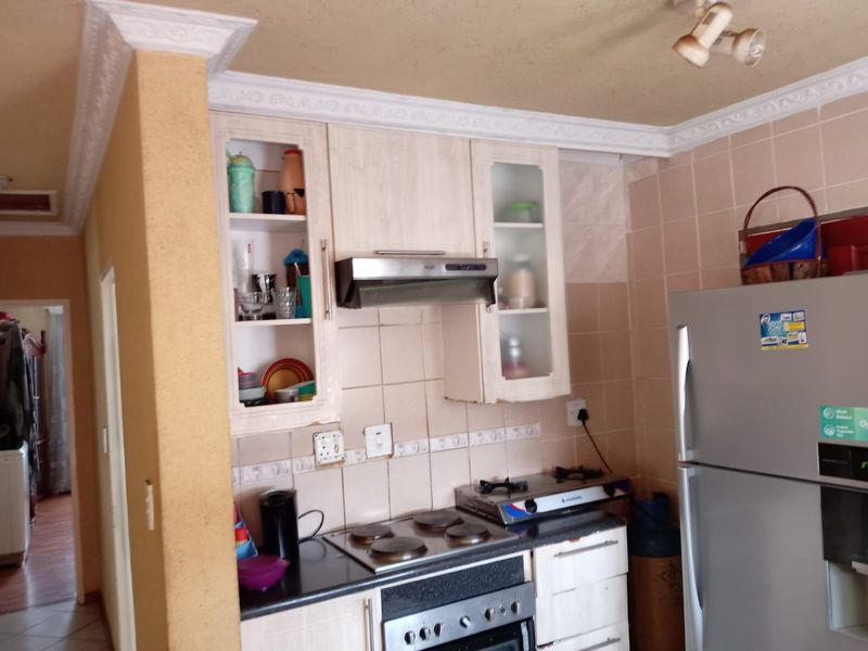 A compact kitchen featuring built-in cabinetry, a hob, an oven, and an extractor fan, with tiled backsplash and decorative ceiling cornicing.