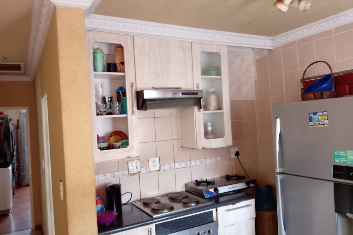 A compact kitchen featuring built-in cabinetry, a hob, an oven, and an extractor fan, with tiled backsplash and decorative ceiling cornicing.