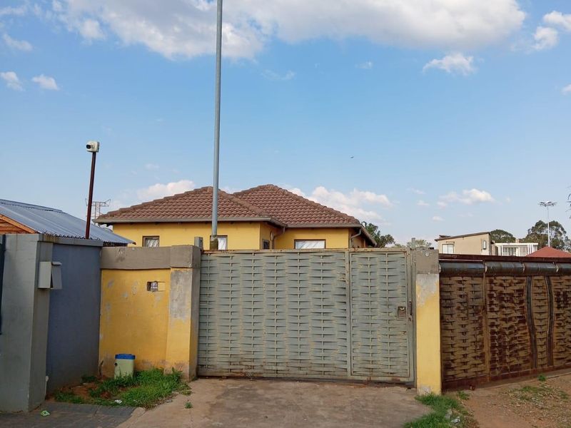 Front view of the property featuring a metal driveway gate, perimeter wall, and tiled roof structure.