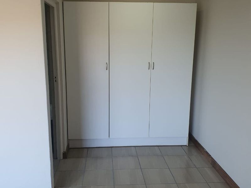A clean, empty bedroom featuring neutral tiled flooring, a built-in white wardrobe, and simple ceiling lighting.