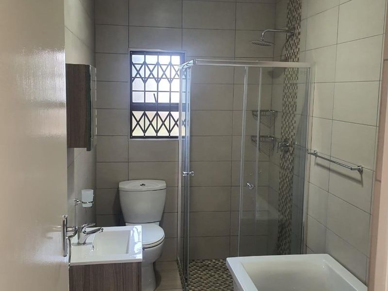 A modern, well-maintained bathroom featuring a separate shower enclosure, bathtub, vanity cabinet with basin, and neutral floor-to-ceiling tiling.