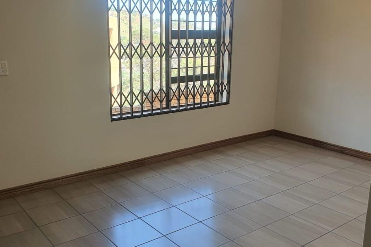 A clean, empty bedroom featuring neutral tiled flooring, a security gate on the window, and a central ceiling light fixture.