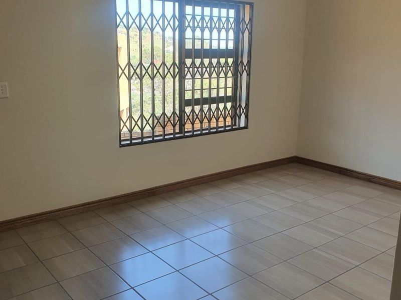 A clean, empty bedroom featuring neutral tiled flooring, a security gate on the window, and a central ceiling light fixture.
