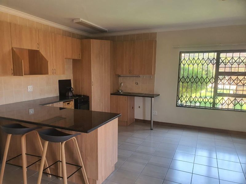 Functional kitchen featuring laminate cabinetry, granite countertops, tiled flooring, and a window with security bars, offering a practical layout for daily use.