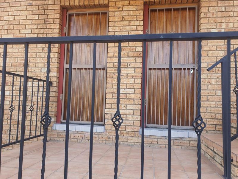 A covered patio area featuring face brick walls, tiled flooring, and secure wrought iron railings with matching security gates over wooden doors.