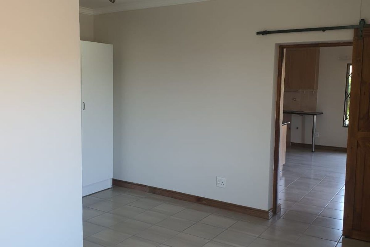 An empty living area featuring tiled flooring, a sliding barn door, and a built-in cupboard, with a view into the adjacent kitchen space.