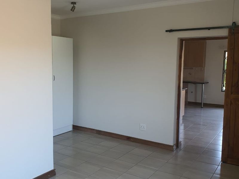 An empty living area featuring tiled flooring, a sliding barn door, and a built-in cupboard, with a view into the adjacent kitchen space.