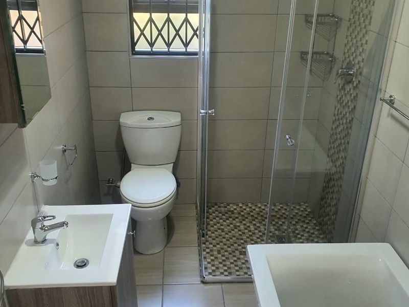 A modern, well-maintained bathroom featuring a glass shower enclosure, a bathtub, a vanity unit, and neutral floor-to-ceiling tiling.