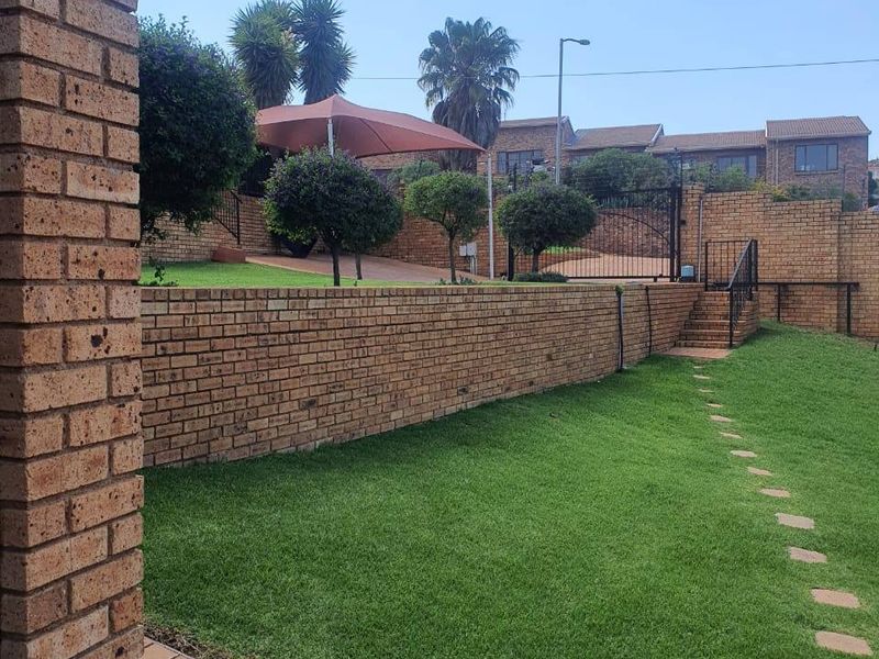 A well-maintained garden area featuring a brick retaining wall, paved pathway, and secure gated access to the upper level.