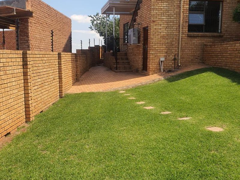 A well-maintained rear exterior view of the apartment featuring a face brick facade, paved patio area, and a neat lawn with secure boundary walls.