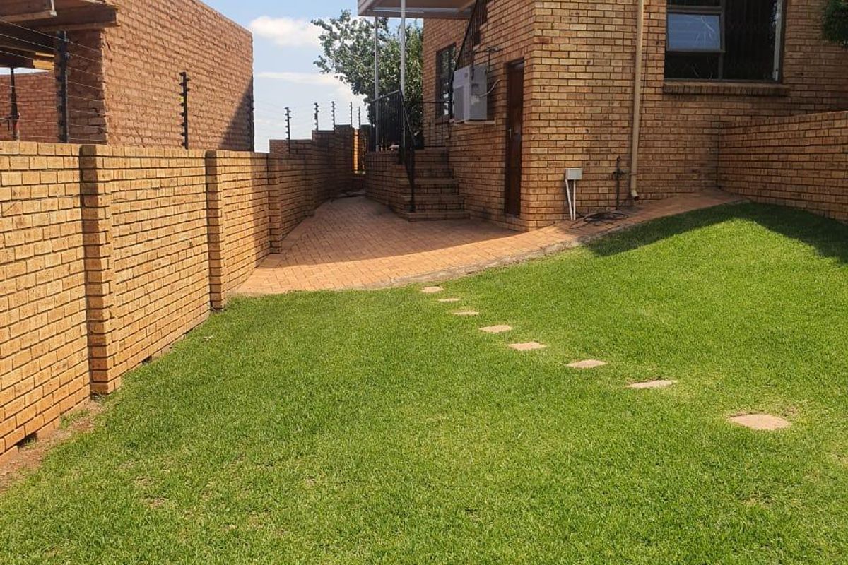 A well-maintained rear exterior view of the apartment featuring a face brick facade, paved patio area, and a neat lawn with secure boundary walls.