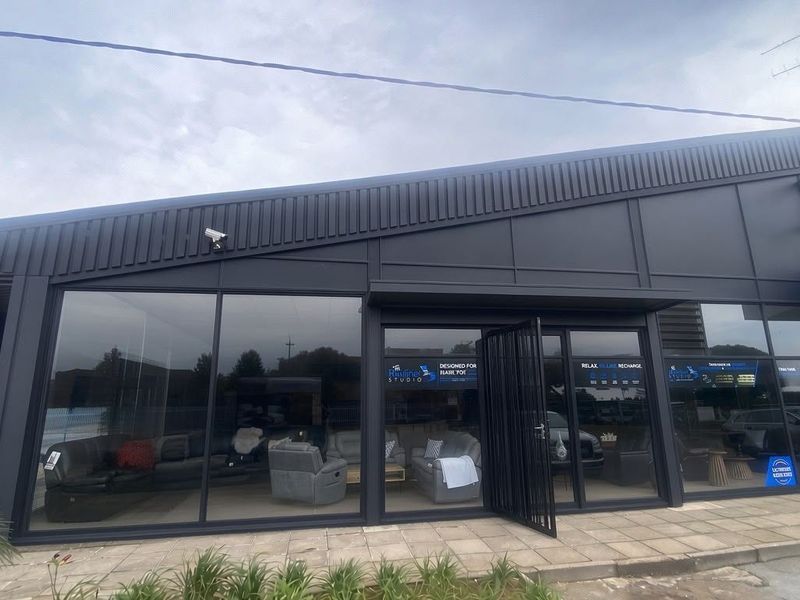 Modern commercial storefront featuring a dark metal facade, expansive glass windows, and a paved entrance area, suitable for retail or showroom use.