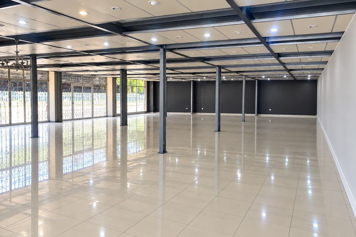 Expansive open-plan commercial space featuring polished tile flooring, exposed steel structural columns, and a modern suspended ceiling with integrated recessed lighting.