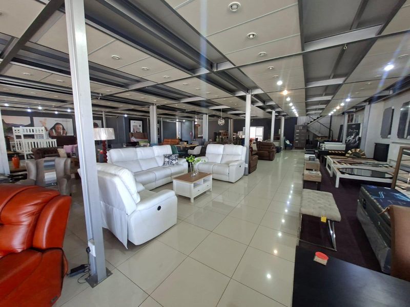 Spacious open-plan commercial showroom featuring high ceilings with exposed steel beams, recessed lighting, and polished tiled flooring.