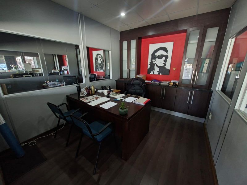 A professional office space featuring dark wood built-in cabinetry, glass-fronted storage units, laminate flooring, and an internal glass partition for a modern commercial layout.