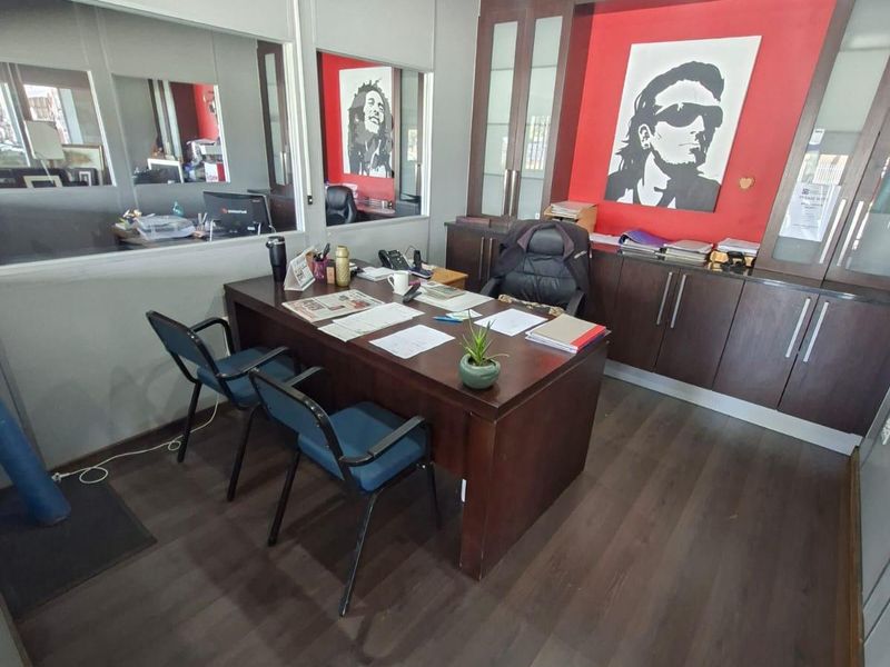 A professional office space featuring dark wood laminate flooring, built-in cabinetry, and a glass partition wall, providing a functional and structured work environment.