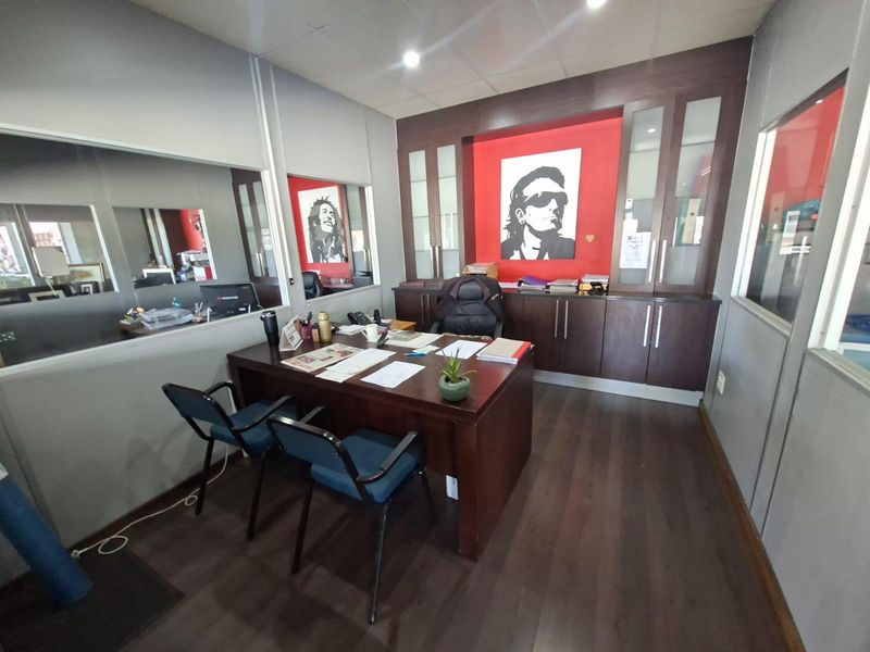 A professional office space featuring dark wood-tone built-in cabinetry, laminate flooring, and glass partition windows providing a bright and functional workspace.