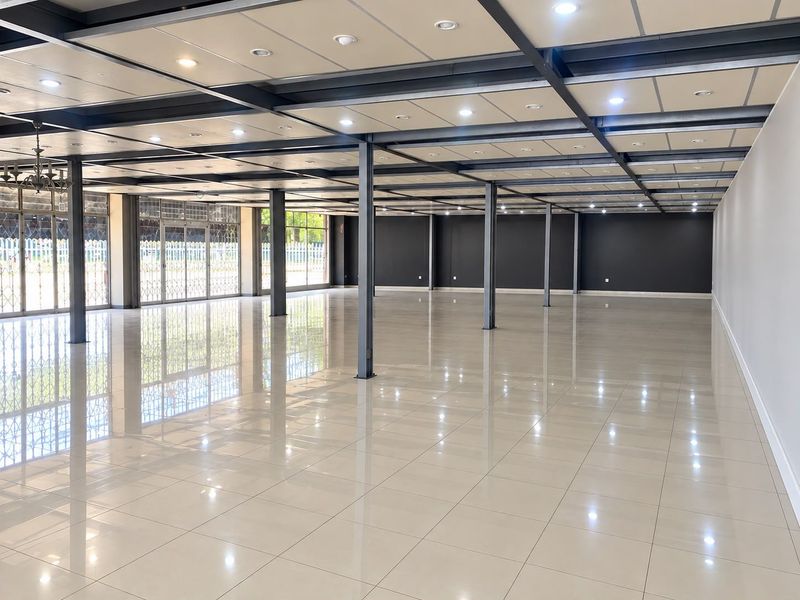 Expansive open-plan commercial space featuring polished tile flooring, exposed steel structural columns, and a modern suspended ceiling with integrated recessed lighting.