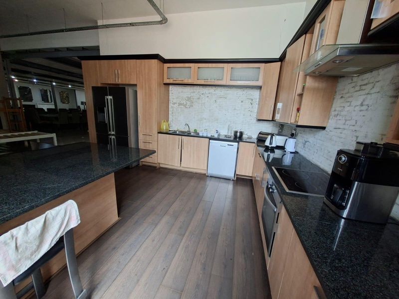Spacious commercial kitchen featuring granite countertops, wood-finish cabinetry, integrated appliances, and an exposed brick backsplash, offering a functional workspace.