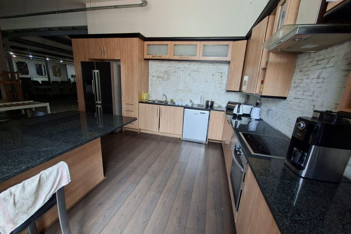 Spacious commercial kitchen featuring granite countertops, wood-finish cabinetry, integrated appliances, and an exposed brick backsplash, offering a functional workspace.