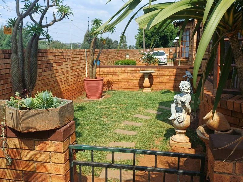 A private garden area featuring a brick boundary wall, a metal pedestrian gate, and a stone paver path leading through the lawn.