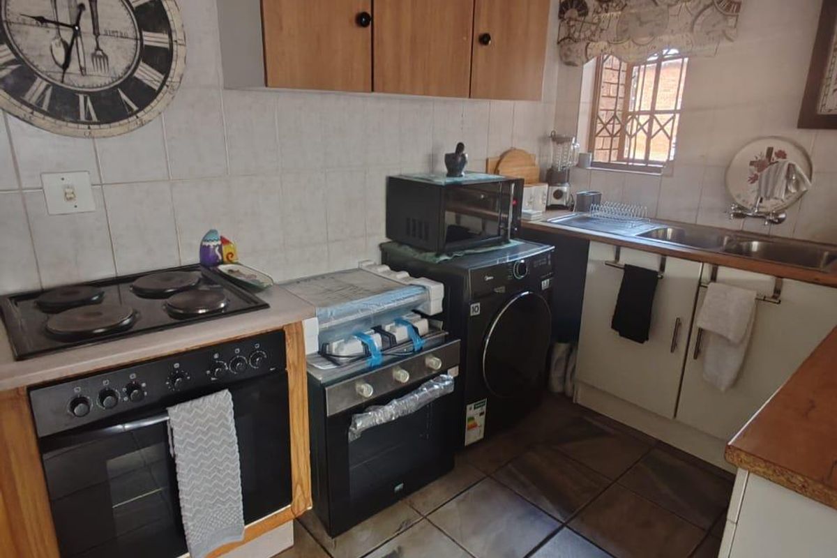 A functional kitchen featuring built-in oven, electric hob, double sink, and tiled finishes, offering a practical layout with ample storage cabinetry.