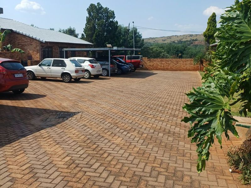 Spacious paved driveway area featuring a covered carport and brick boundary wall, providing ample parking space for multiple vehicles.