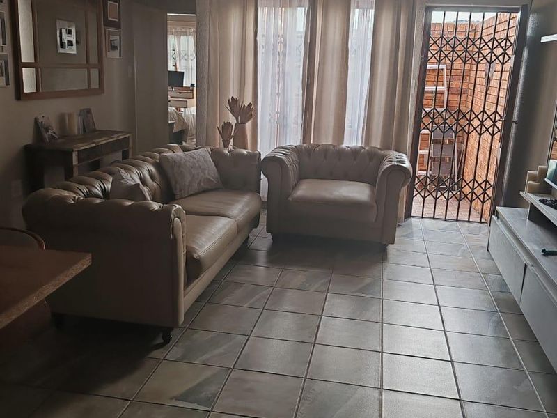 A living room featuring tiled flooring, a ceiling light fixture, and a sliding glass door leading to a secure outdoor area.