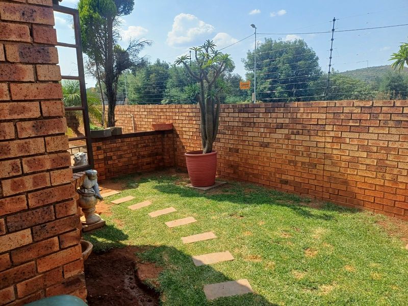 A private garden area featuring a brick boundary wall with integrated electric fencing and a stone paver pathway set within a lawn.