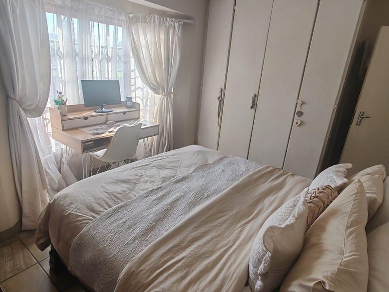 A cozy bedroom featuring built-in cupboards, tiled flooring, and natural light from a large window.