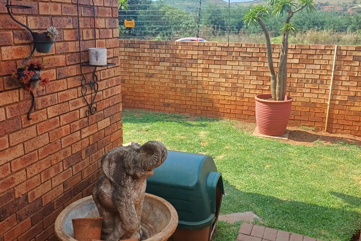 A private rear garden featuring a face brick wall, paved walkway, and secure perimeter walling with electric fencing.