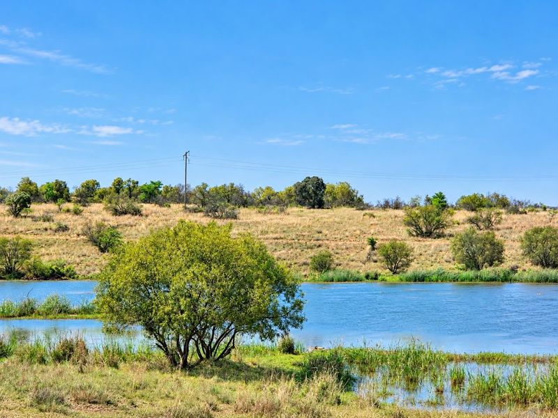 A scenic view of a tranquil river flowing through the farm landscape, showcasing natural vegetation and open terrain.