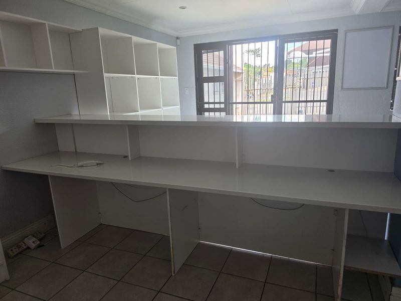 A functional office space featuring a large built-in desk, integrated shelving units, tiled flooring, and a secure entrance with a metal security gate.