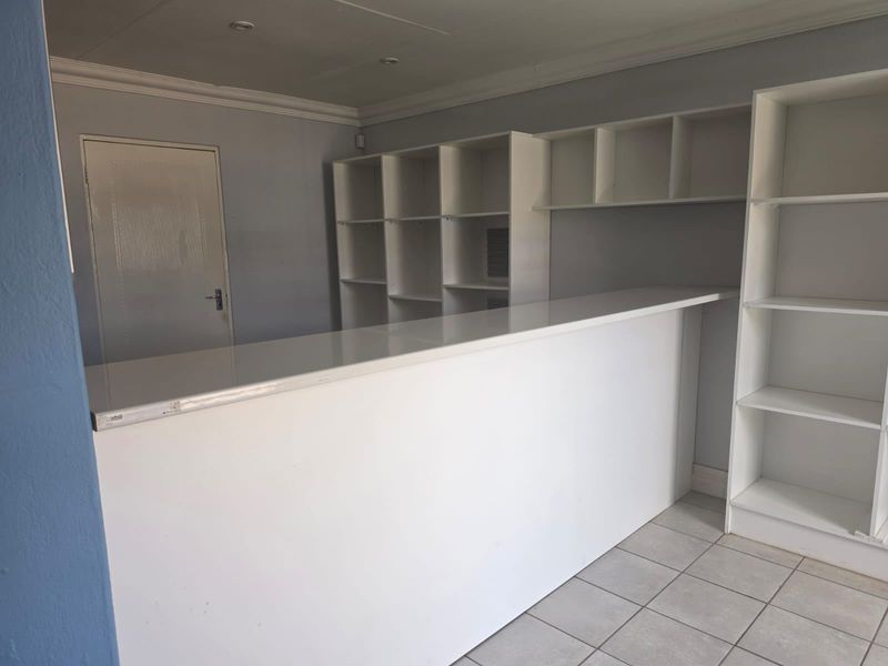 A functional commercial office space featuring a built-in reception counter, extensive integrated shelving, tiled flooring, and recessed lighting.